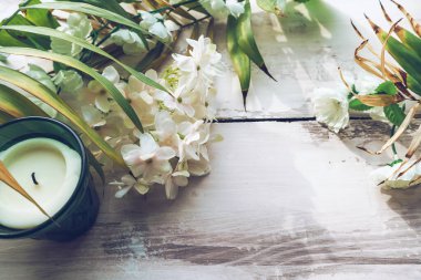 Beyaz ahşap zemin üzerinde uzanan mum, palmiye yaprakları ve beyaz çiçeklerin üst görüntüsü
