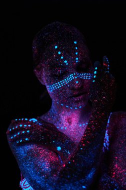 Sanat kadını ultraviyole ışıkta kozmos. Bütün vücudu renkli damlacıklarla kaplı. Karanlıkta poz veren kız. Gürültü, odak dışı