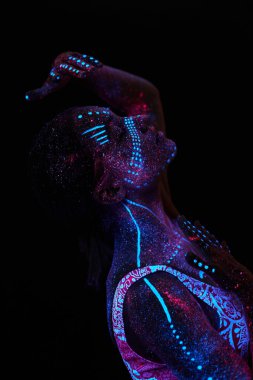 Sanat kadını ultraviyole ışıkta kozmos. Bütün vücudu renkli damlacıklarla kaplı. Karanlıkta poz veren kız. Gürültü, odak dışı