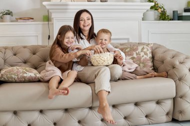 Annem oğlu ve kızıyla kanepede oturup film izliyor. Bir kadın, bir oğlan ve bir kız film izlerken patlamış mısır yer. Aile hafta sonları evde dinleniyor.