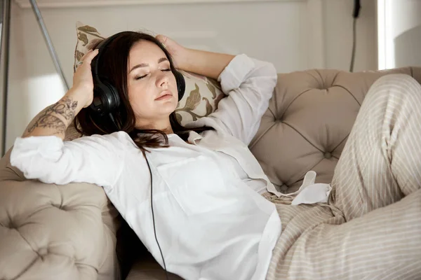 女人躺在家里的沙发上 带着耳机听音乐 在家休息一天 休息一下 — 图库照片