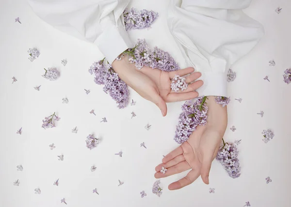 Natural woman cosmetics for hands made of lilac flowers and petals. Moisturize and soften the skin of the hands. Lilac flowers protrude from the sleeves of the arm