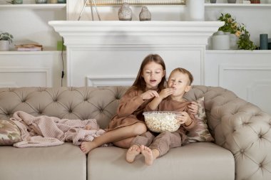 Erkek ve kız kardeş kanepede oturmuş patlamış mısır yiyorlar. Bir erkek ve bir kız rahatlar ve TV 'de film izlerler.