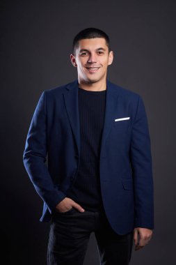 Stüdyoda koyu arka planda mavi ceketli bir iş adamının portresi. Kısa saçlı Mulatto adam. Genç kendine güvenen yönetici gülümsüyor