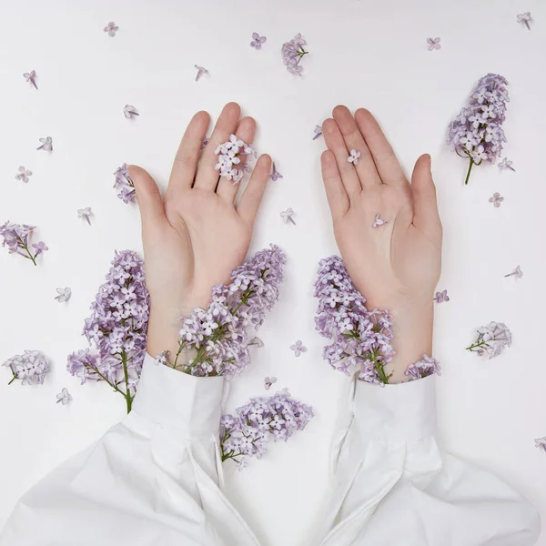 Natural woman cosmetics for hands made of lilac flowers and petals. Moisturize and soften the skin of the hands. Lilac flowers protrude from the sleeves of the arm