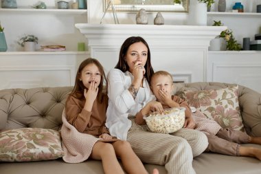 Annem oğlu ve kızıyla kanepede oturup film izliyor. Bir kadın, bir oğlan ve bir kız film izlerken patlamış mısır yer. Aile hafta sonları evde dinleniyor.