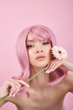 Pembe boyalı, güçlü saçları olan romantik bir kadın pembe arka planda elinde çiçek tutuyor. Doğal renkli saçlar güzel makyaj, güçlü kökler.