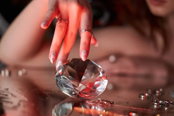 Beauty Woman holds big diamond in hand while lying on table. Beautiful hands, professional manicure, large brilliant