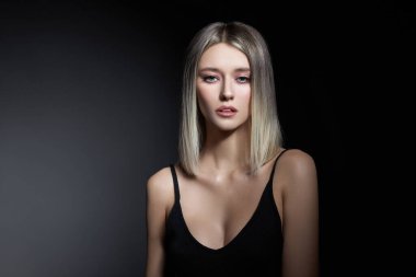 Siyah arka planda sarı saçlı bir kadın. Saç modelini kül rengine boyamak. Bir kızın portresi.