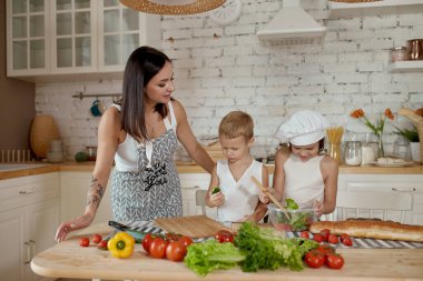 Çocuklar mutfakta vejetaryen salatası yapmayı öğrenirler. Aile tatili, kendi ellerinle öğle yemeği. Anne ve genç aşçılar vejetaryen yemekleri pişiriyor.