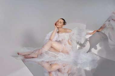 Açık şeffaf elbiseli romantik güzel kadın yerde oturan esnek bir aynaya yansıyor. Mükemmel vücut ve uzun bacaklar.