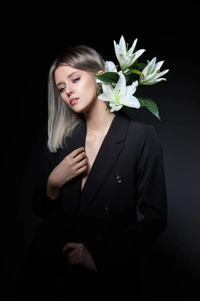 Woman colored hair color of a blonde with lily flower on black background. Coloring hair woman model in ash color. Portrait of a girl