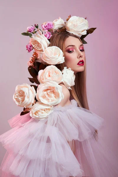 美容女性の明るい赤化粧 頭の女性にバラの花 ピンクの背景に透明な光のドレスを着たアートガール プロの明るいメイク — ストック写真