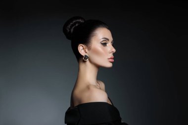 Koyu arkaplanda akşam makyajı yapılmış klasik bir kadın portresi. Kırışıklıkları olmayan mükemmel bir cilt, profesyonel güzellik makyajı, uzun kirpikleri. Siyah elbiseli mükemmel kız.