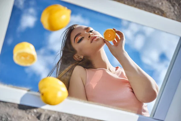 Woman with a lemon in her hands, beauty skin nutrition with vitamin C. Natural cosmetics for facial skin care. Sunny day blue sky