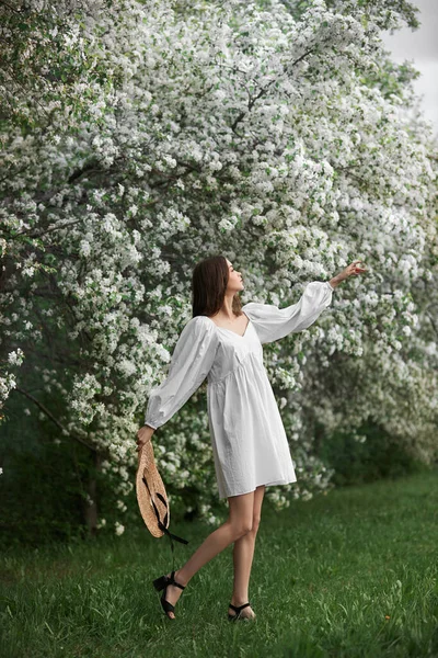 Ung Kvinna Vit Klänning Med Halmhatt Går Genom Blommande Vårträdgård — Stockfoto