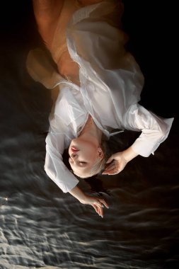 Gün batımında çıplak ve seksi bir kadın. Kısa ıslak saçları ve büyük göğüsleri olan güzel sarışın kadın, denizdeki sanat portresi