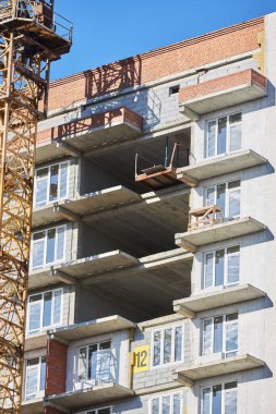 construction site showcases a residential building with exposed floors and balconies. crane stands nearby as workers prepare for installation and finishing tasks.