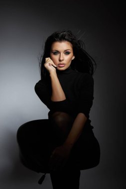 confident model strikes a pose in a dimly lit studio, showcasing her flowing hair and stylish outfit. soft background enhances the focus on her expressive features and attitude.