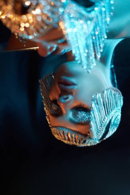 Model, sanatsal bir ışığı yansıtan parıldayan boncuklarla süslenmiş zarif bir başlık sergiliyor. arka plan yumuşak renklerle çelişiyor, görüntünün güzelliğini ve yaratıcılığını arttırıyor.