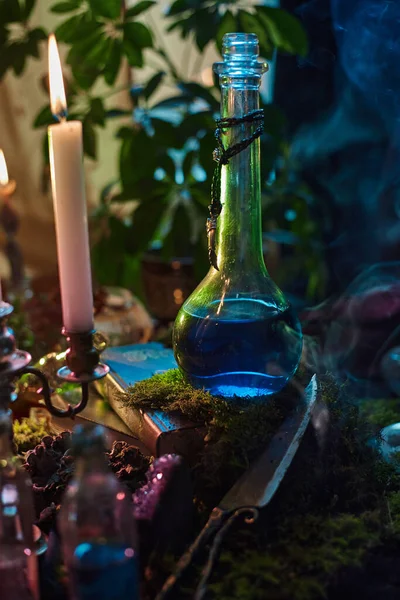 Mavi iksir, ahşap bir masada cam bir şişenin içinde duruyor. Mumlar yanıp sönüyor, gölgeler düşüyor. ayar bitkiler ve diğer mistik nesnelerle doludur, büyülü bir atmosfer yaratır..