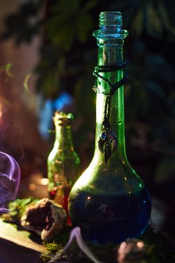 Karanlık çevrede ilgi çekici sıvılarla dolu iki renkli cam şişe bulunur. Çevreleyen elementler arasında bitkiler ve bir tutam duman vardır, büyüleyici bir atmosfer yaratırlar..