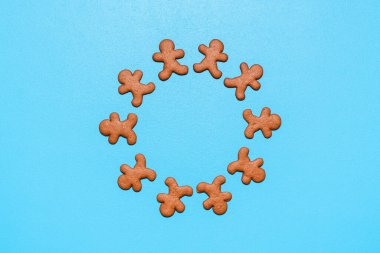 Mavi arka planda zencefilli kurabiye. Kurabiyeler bir masanın üstünde daire şeklinde dizilmiş, düz uzanmış.