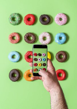 Bir adamın eliyle yukarıda akıllı telefonuyla jöleli donutları fotoğraflıyor. Telefonla yemek fotoğrafçılığı..