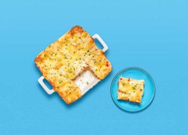 Mavi bir masada ev yapımı vejetaryen lazanyası. Bir tepsi taze pişmiş lazanya ve tabakta bir porsiyon