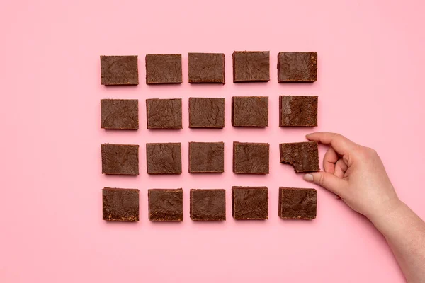 用一个女人的手抓起一块巧克力软糖蛋糕的头像 平躺在粉红的背景上 对称地排列着几块巧克力软糖 — 图库照片