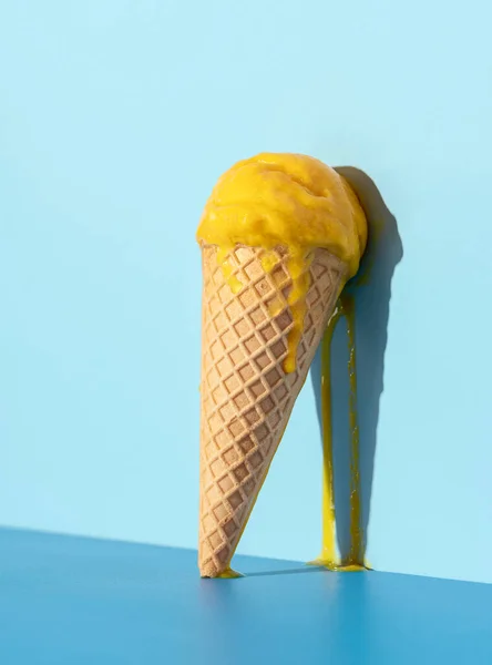 Melted mango ice cream dripping on a blue wall. Mango ice cream in a waffle cone in bright light