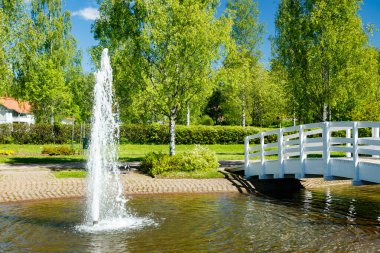 Güneşli bir yaz gününde göleti, ahşap köprüsü ve çeşmesi olan güzel bir park.