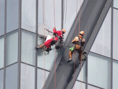 Pencere temizleyicileri Yangon, Myanmar 'da yüksek bir binanın dış tarafındaki halatlarla asılı dururken yükseklikte çalışırlar..