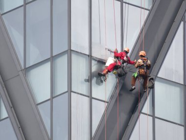 Pencere temizleyicileri Yangon, Myanmar 'da yüksek bir binanın dış tarafındaki halatlarla asılı dururken yükseklikte çalışırlar..