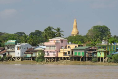 Myanmar 'da bir nehir kıyısında renkli evler ve altın pagoda.