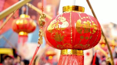 Altın süslemelerle süslenmiş göz kamaştırıcı kırmızı bir Çin feneri canlı bir şenlik atmosferinde asılı duruyor, neşe ve kutlama duyguları uyandırıyor. Kültürel etkinlikler, festivaller ve geleneksel dekorlar için mükemmel..