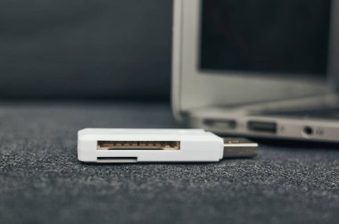 Pürüzsüz beyaz bir USB kart okuyucusu dizüstü bilgisayarı tamamlıyor. Teknoloji meraklıları ve aksesuar severler için ideal.