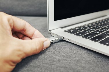 Biri USB belleği bir dizüstü bilgisayara takıyor. Laptop gri bir yüzeyde.