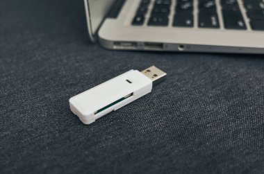 Pürüzsüz, kompakt beyaz bir USB flaş bellek koyu renkli, şık bir arka planda dizüstü bilgisayarın yanına yerleştirilir.