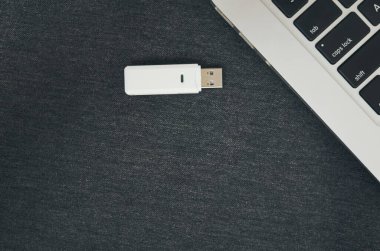 Parlak gümüş bir dizüstü bilgisayarın yanında duran parlak beyaz bir USB bellek koyu renkli bir yüzeyde modern bir sahne yaratıyor.