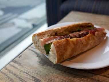 Etli baget, tabakta salatalık, pencerenin yanındaki ahşap masa, bulanık sokak manzarası, şehir manzarası.