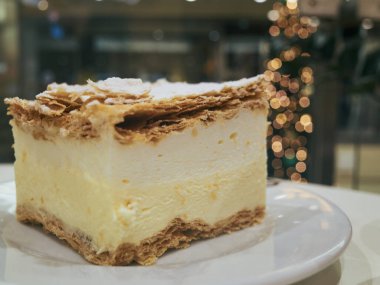 Beyaz tabakta kremalı pasta dilimi, katmanlı krema ve çıtır çıtır altın pudra şekerle tozlanmış hamur işi arasında çırpılmış krema.,