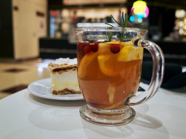 Sıcak narenciye çayı kremalı pasta, yazarın öğle arası rahat bir kafede, portakal dilimleri ve kızılcıklarla dolu cam bardak.,