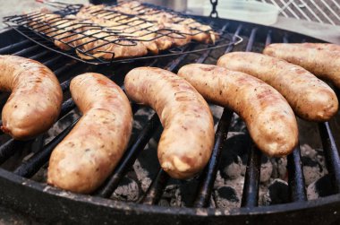 Barbekü ızgarasında pişen cızırtılı sosisler, yaz toplantıları ve harika açık hava yemekleri için ideal bir ikram.