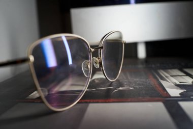 Ekran ışığıyla aydınlatılmış altın gözlük lenslerde serin mavi yansıma, gece odaklı iş akışı. Metal çerçeve ve mercek kaplama