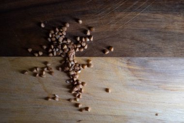 Dökülen karabuğday filizleri koyu ahşap tahtaya saçılmış, yüksek kontrastlı karabuğday aydınlatması dokunsal yaratıyor.