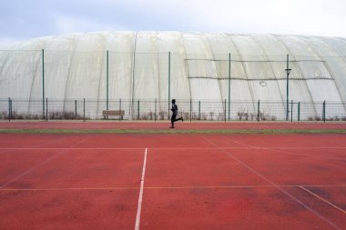 Geniş kırmızı yolda koşan Kubbe 'ye karşı, küçük siluet şeritleri sabit adımlarla, geometrik