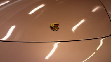 Beige Porsche Hood Emblem CloseUp Showing Refined Glossy Finish, Heritage Crest And Soft Ceiling Light Warsaw, Poland