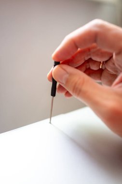 Kapalı parmaklar dizüstü bilgisayarda tornavida tutuyor, ucu ve vidaya seçici odaklanma, yumuşak nötr arkaplan,