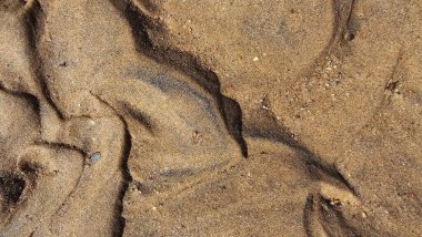 Kumsal kum dokusu. Geniş, dalgalı, kısa yatay çizgiler, dalgalanmalar ve rüzgarın oluşturduğu desenlerle dokulu bir kum yüzeyinin yakın çekimi. Renkler ışıktan koyu kahverengiye değişir.